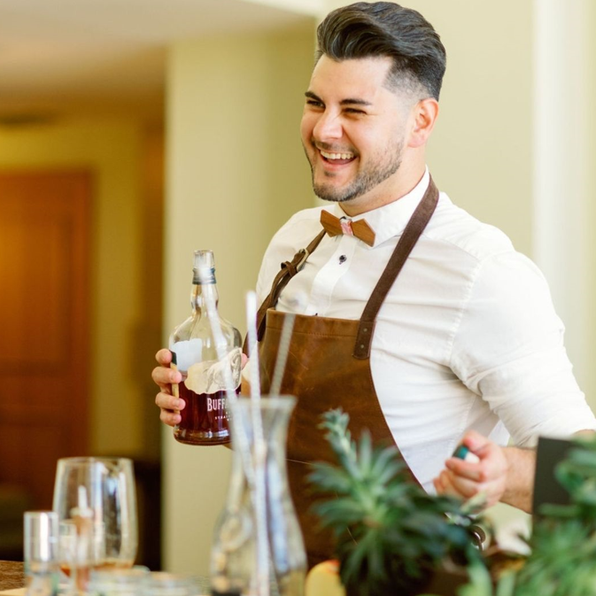 Arthur Plowden, owner of Bar Artistry, mixing a drink at an attractive bar with a big smile and open expression.