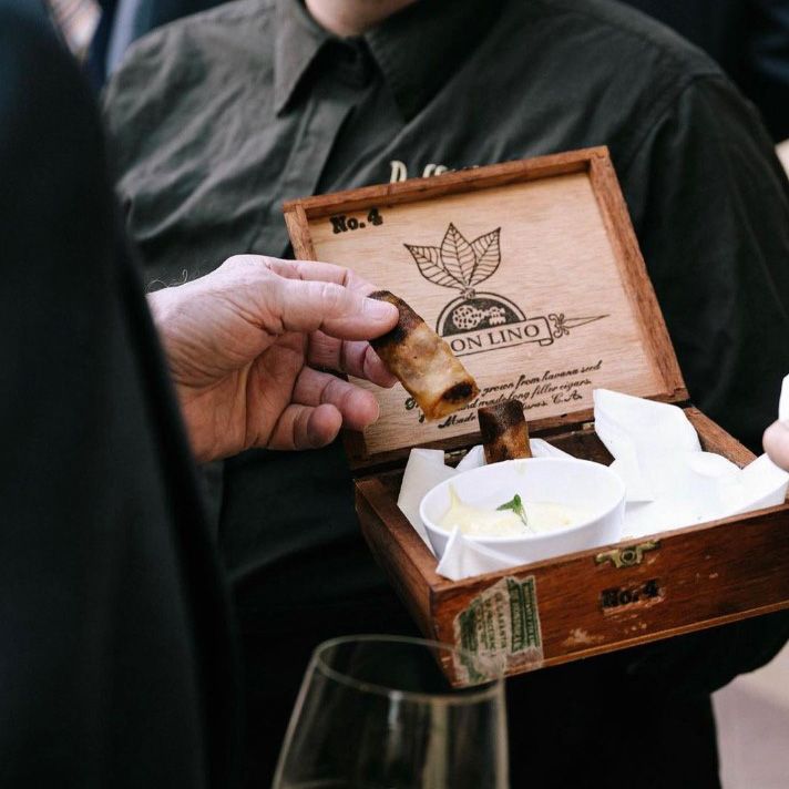 a food server wearing a black shirt offering a cigar box with egg rolls inside with a dipping sauce