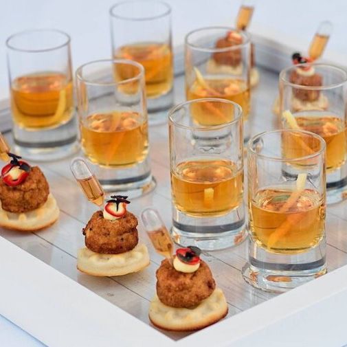 image of small crabcakes and whit glasses filled with a brown liqueur with orange rinds on a white framed tray