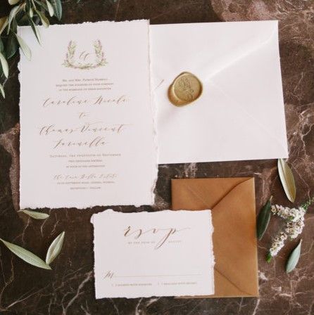 image of wedding stationary show a wedding invitation, envelope, and reply card and reply envelope on a brown rustic background with greenery