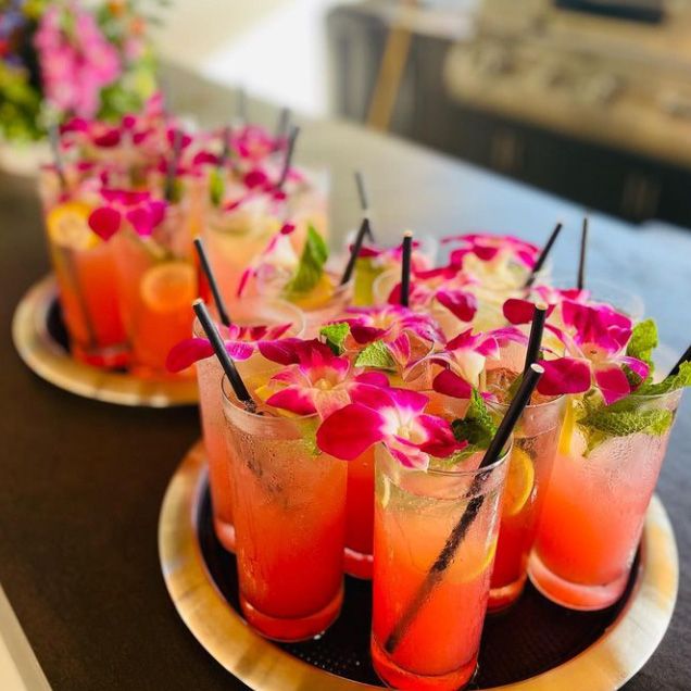 2 gold trays filled with high ball glasses of a tropical pink drink with flowers floating on top