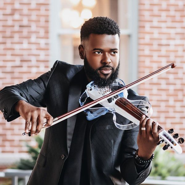 image of a handsome black man in a black suit playing the violin in front of a brink buildingith balsamic sitting upon a wood serving board